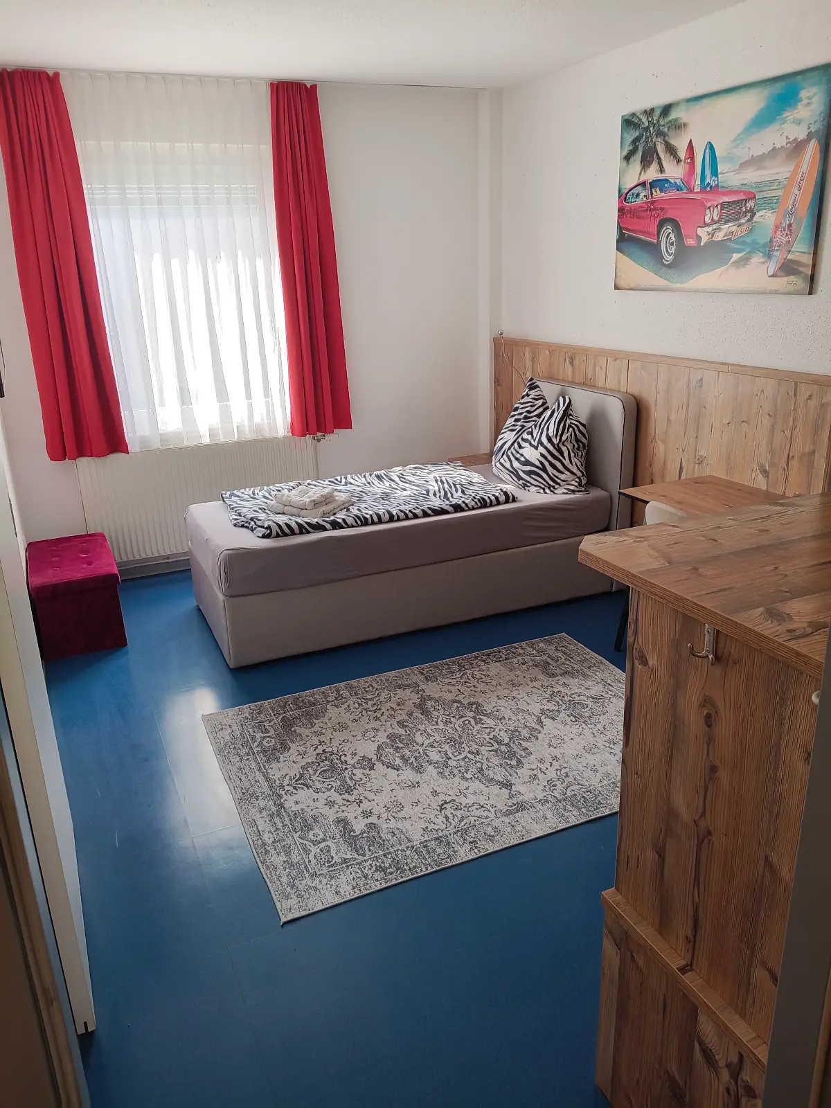Helles Schlafzeit-Einzelzimmer mit Boxspringbett, Holzmöbeln und roten Vorhängen